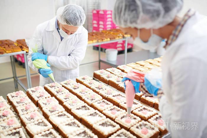 专业patissiers在小糕点中均匀引起彩色奶油的工厂侧面视图